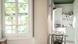 A bright kitchen with white cabinets, a dining table with chairs, and a window with a view of trees. - Brera Apartments in Porta Romana (Milan)