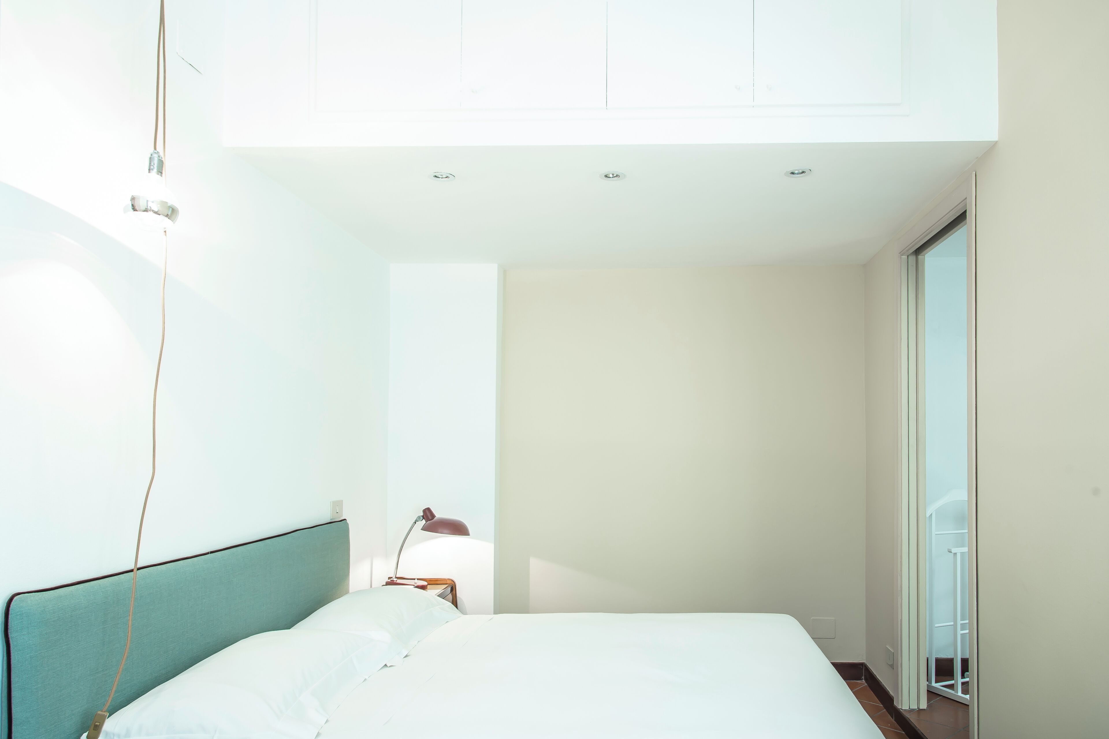 A bedroom with a bed, a desk, and a chair. There is a window and a door.