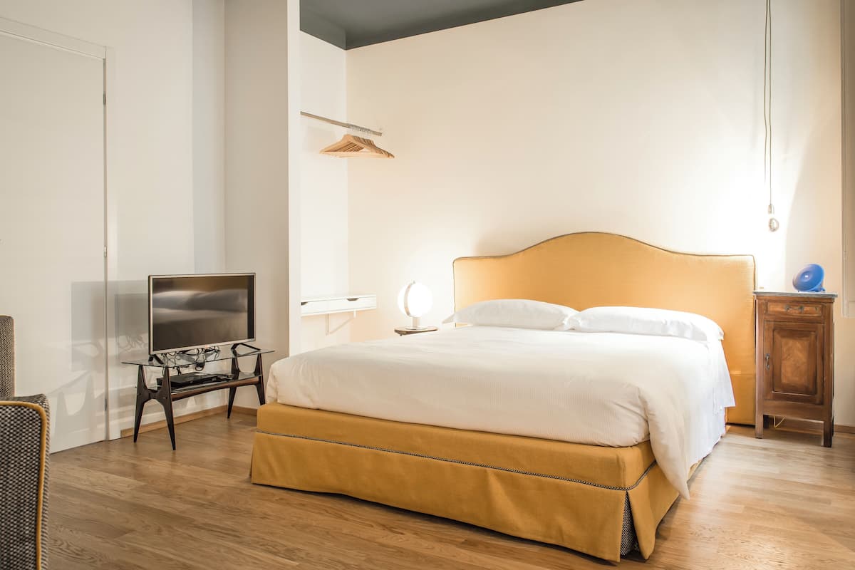 A bedroom with a bed, a TV on a stand, a bedside table, and a wardrobe.