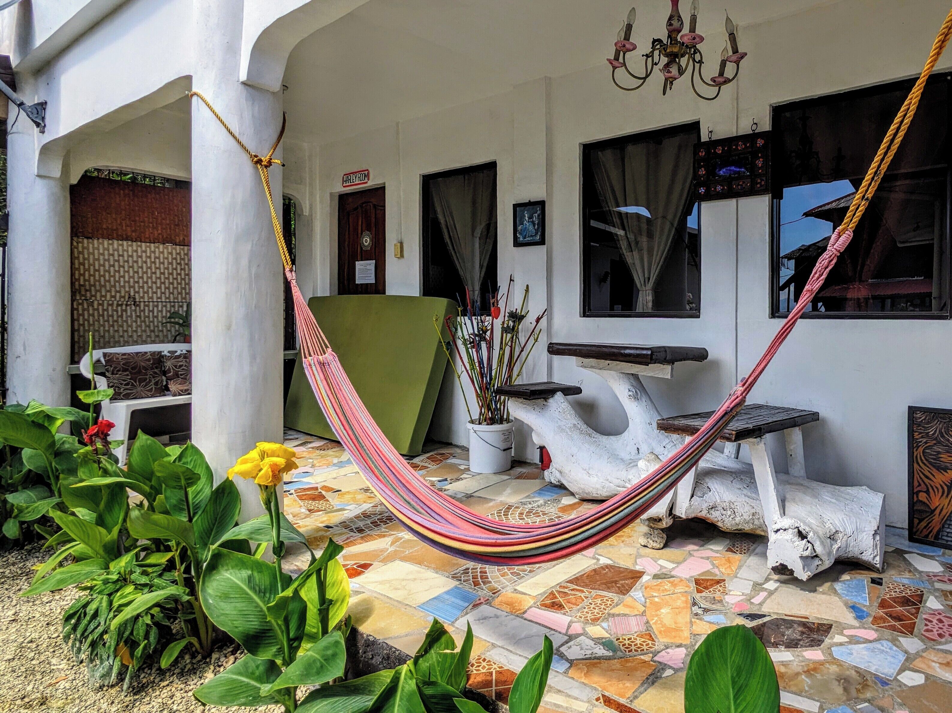 A hammock on a tiled patio with a white wall, a green chair, and a potted plant.