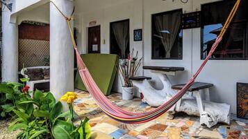A hammock on a tiled patio with a white wall, a green chair, and a potted plant.