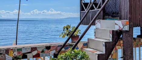Una escalera de madera que conduce a una construcción con techo de paja y una bandera, con vista a un cuerpo de agua.