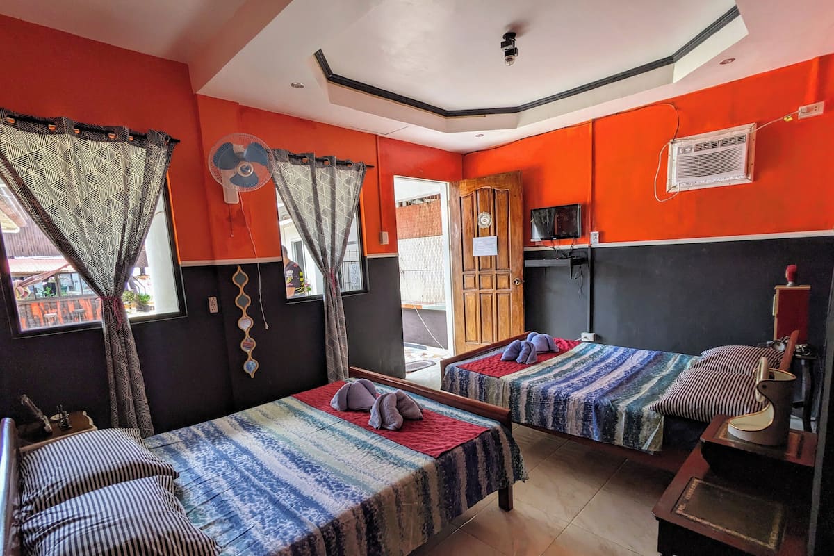 Une chambre avec deux lits, une petite table, un téléviseur et une fenêtre avec des rideaux.