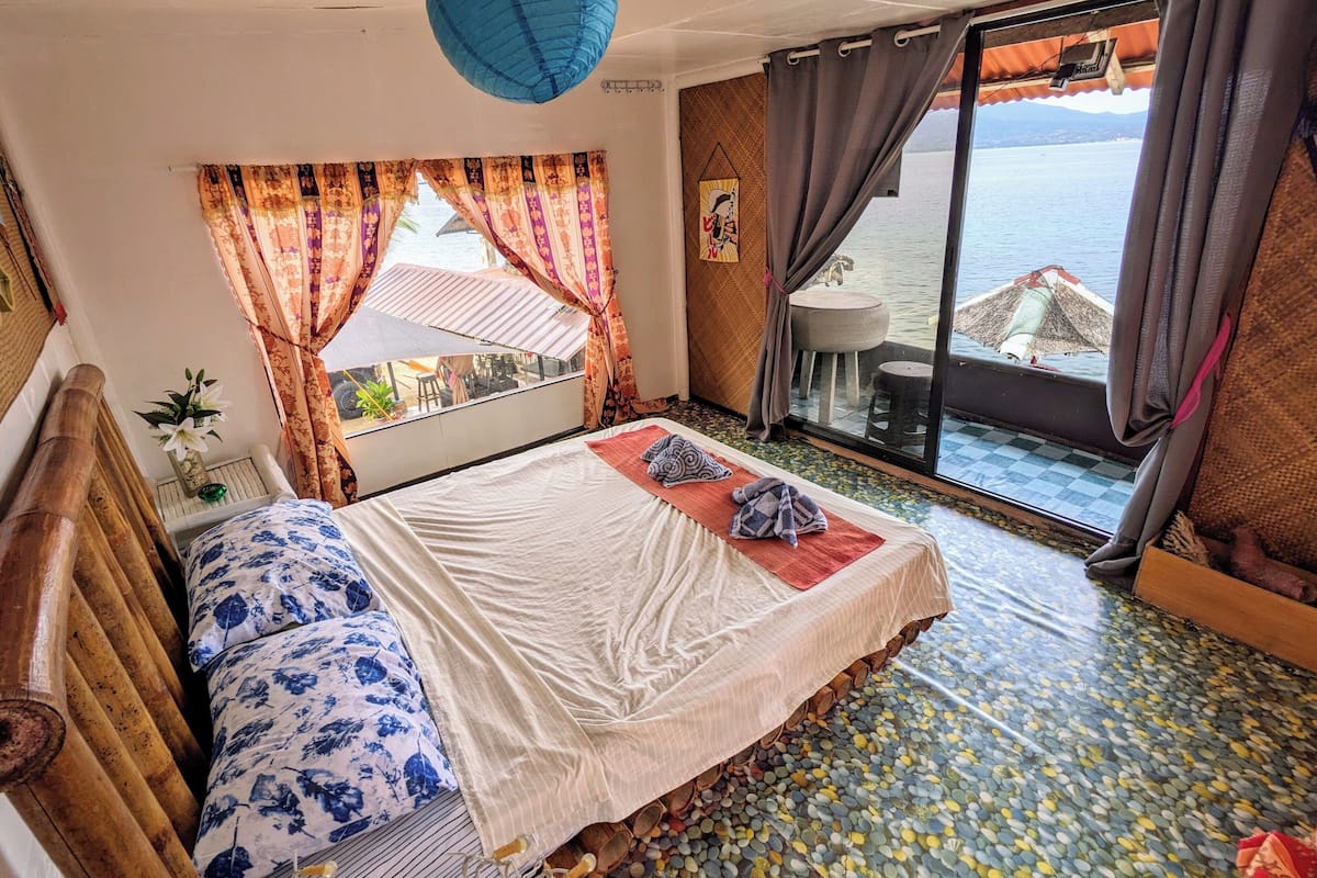 Une chambre avec un lit, une vue sur l’eau et un balcon équipé d’une table et de chaises.