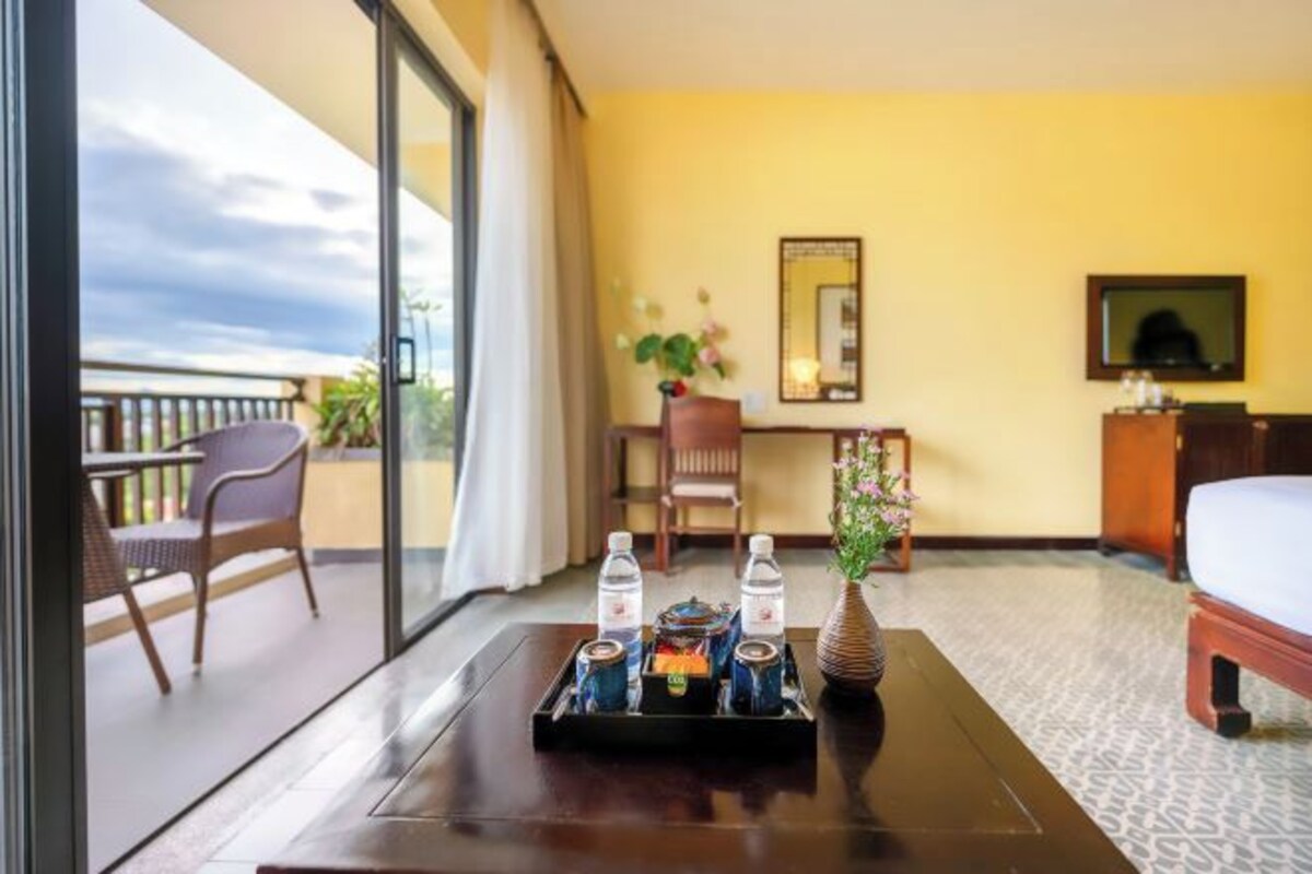 Een hotelkamer met balkon, een bureau met een dienblad stilmineraalwater, een bed en een televisie.