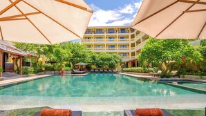 A pool area with lounge chairs and umbrellas, surrounded by lush greenery and a multi-story building in the background. - Hoi An Central Boutique Hotel & Spa (Da Nang)