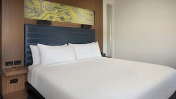 A hotel room with a large bed, a wooden headboard with a circuit board design, a nightstand, and a wall-mounted clock.
