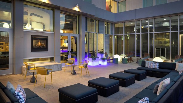 A modern outdoor lounge area with seating arrangements, a fireplace, and large windows. - Aloft by Marriott Wichita (Wichita)