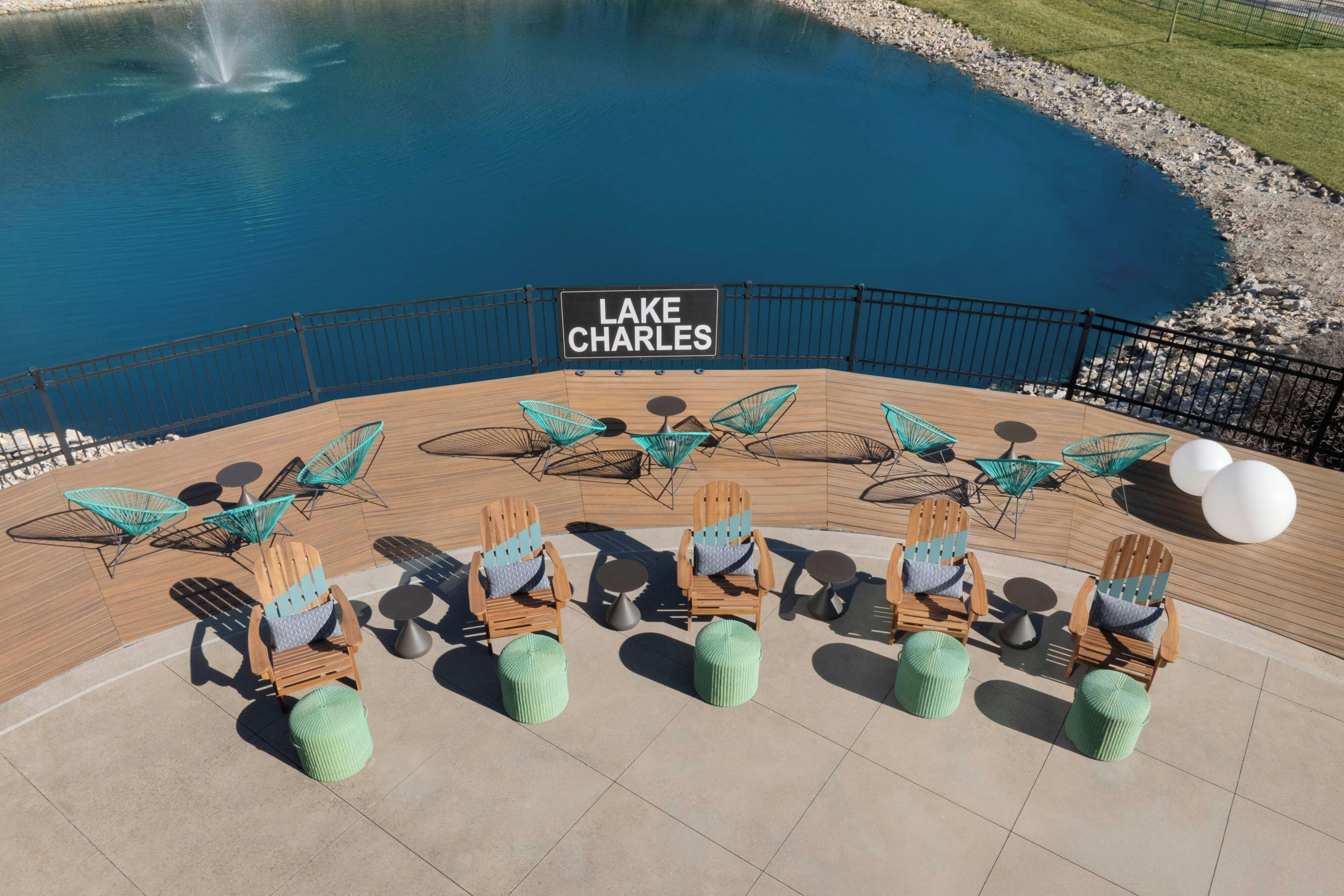 Un área de estar frente al lago con sillas y mesas de madera, un cartel que dice 'LAKE CHARLES' y vistas al lago.