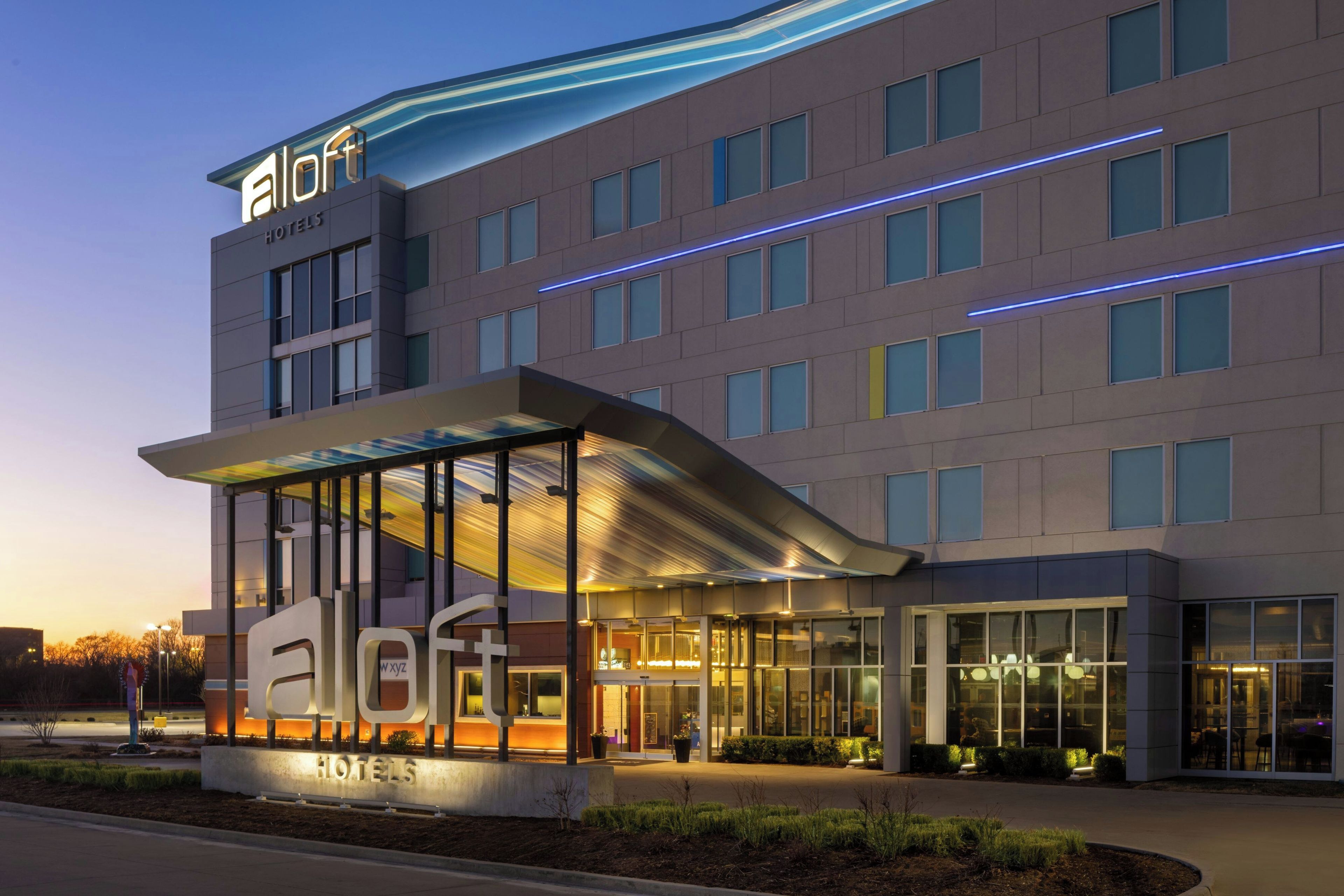 A modern hotel building with a glass facade, a covered entrance, and a sign indicating it is a hotel.