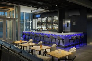 Una zona de bar con mostrador, taburetes y un área de asientos con mesas y sillas.