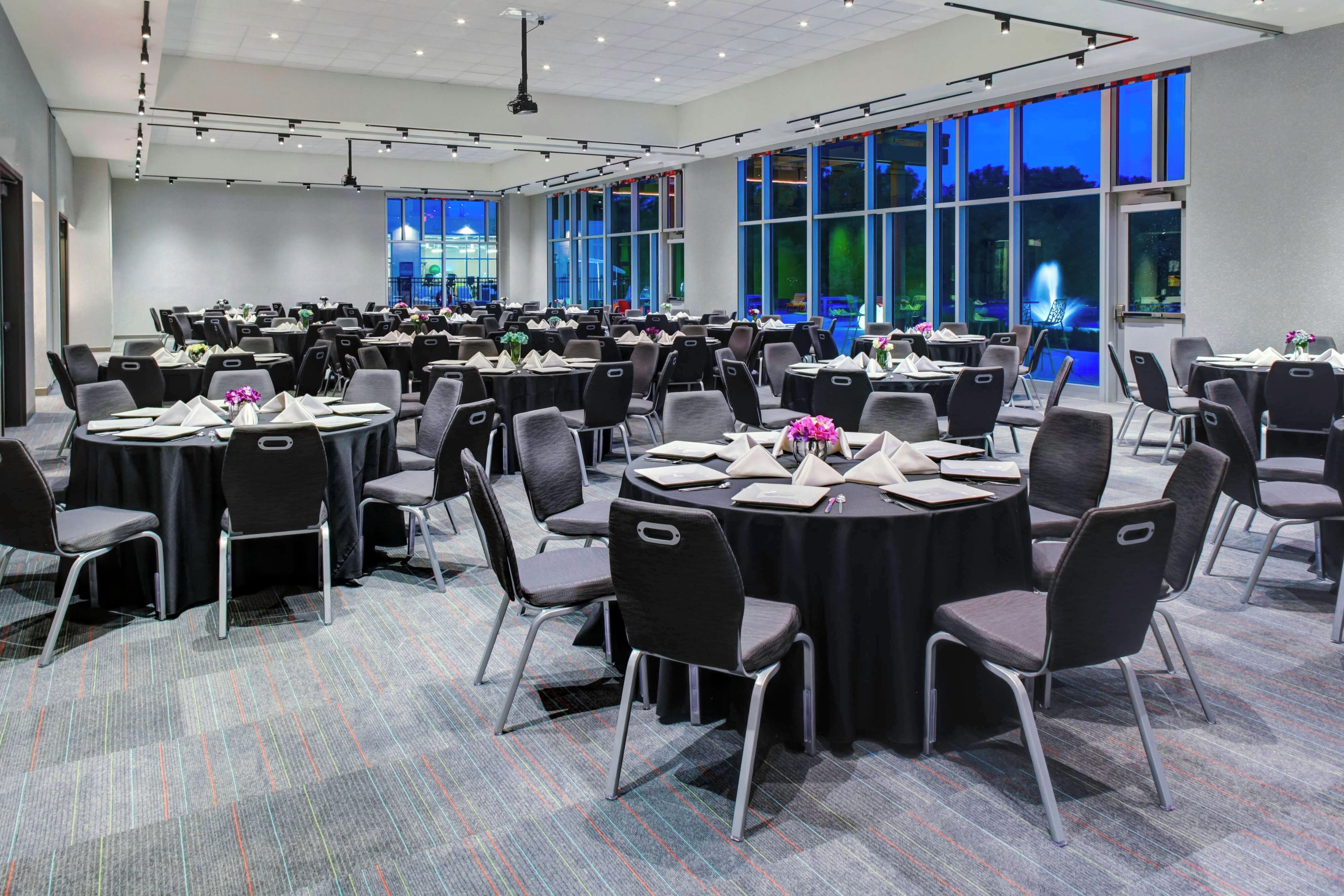A large conference room with multiple round tables, each set with chairs, place settings, and centerpieces.