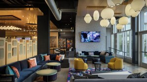 A modern lobby with a long sofa, yellow chairs, and a TV on the wall. - Aloft by Marriott Wichita (Wichita)