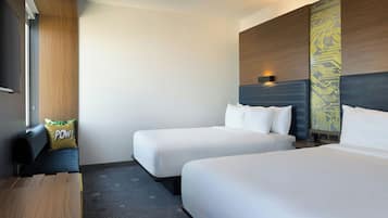A hotel room with two single beds, a desk, and a chair.