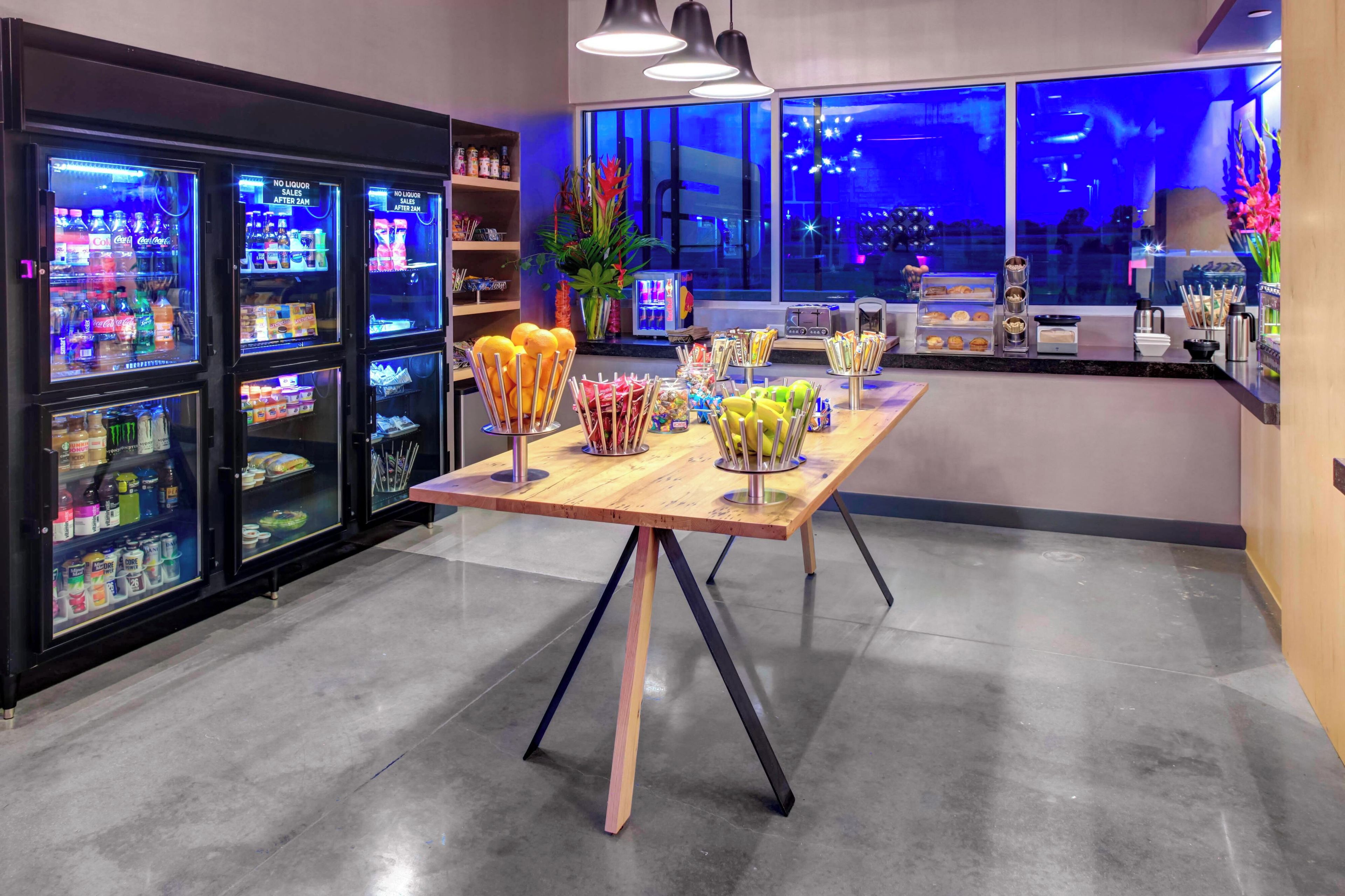 A bar area with a long wooden table, various snack dispensers, and a refrigerator stocked with beverages.