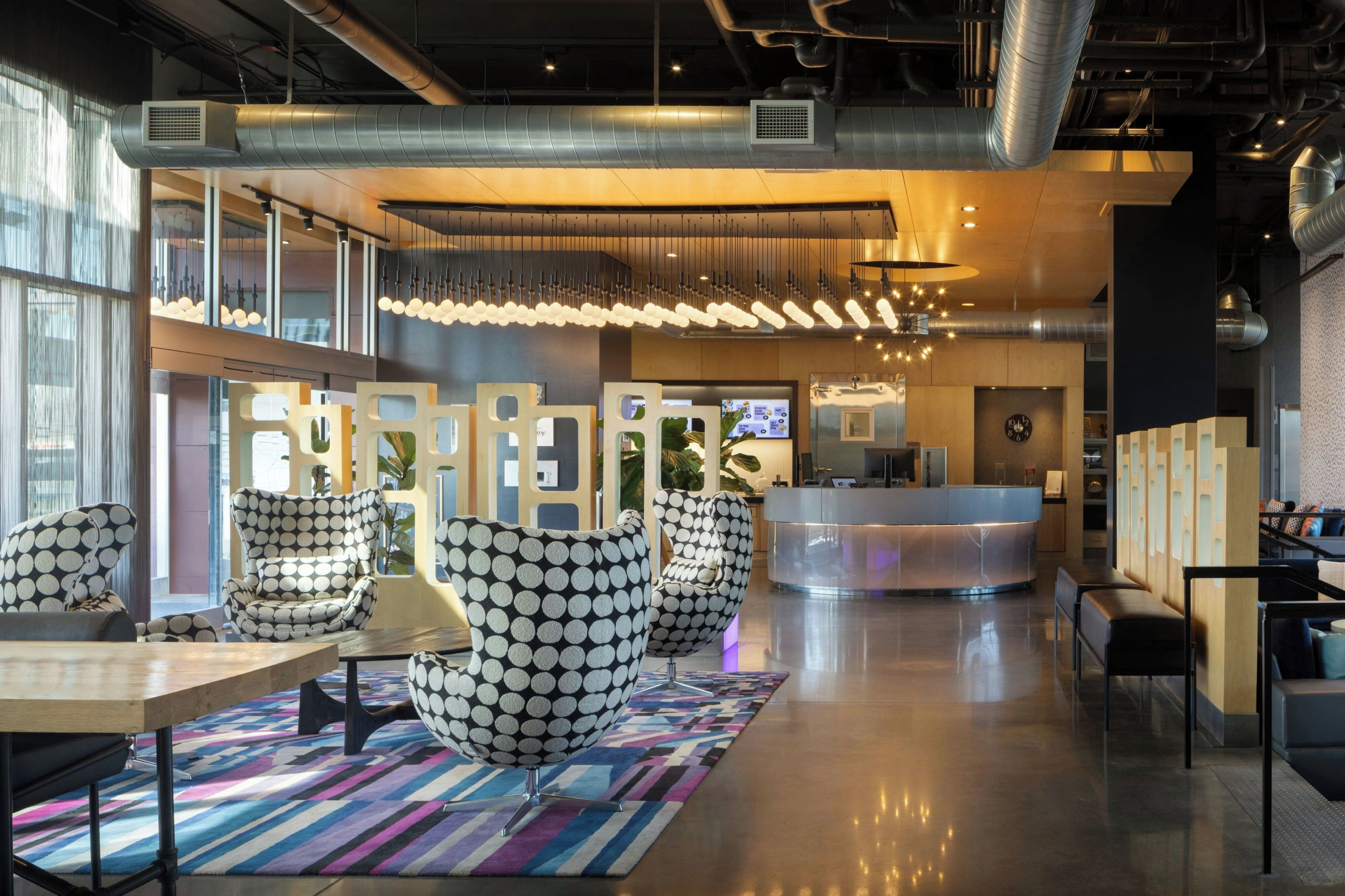A modern lobby with a reception desk, seating area with patterned chairs, and a colorful rug.