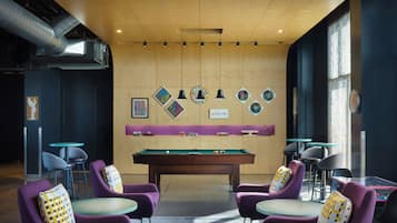 Una mesa de billar en una habitación con sillas moradas y techo de madera.