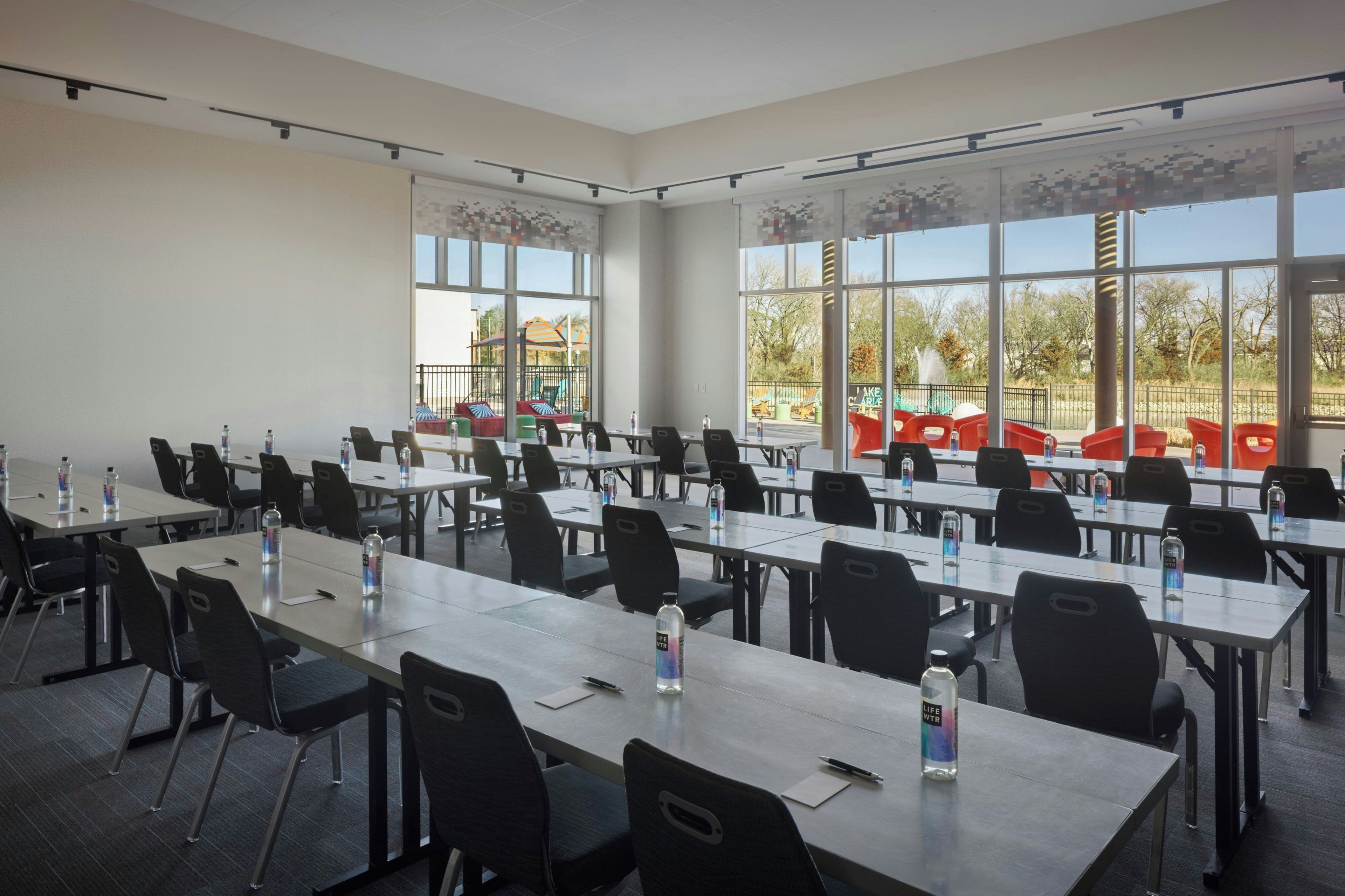 A conference room with multiple tables and chairs, large windows, and a view of an outdoor playground.
