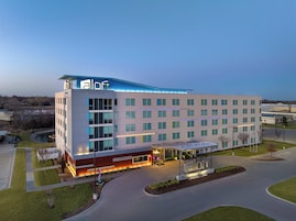 A modern hotel with a flat roof, multiple floors, and a well-lit entrance.