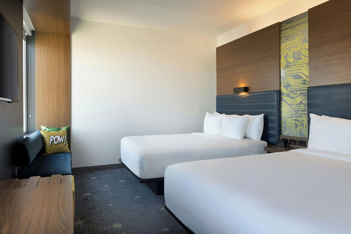 A hotel room with two single beds, a wooden desk, a sofa, and a wall-mounted TV.