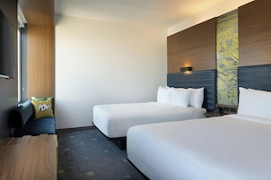 A hotel room with two single beds, a wooden desk, a sofa, and a wall-mounted TV.