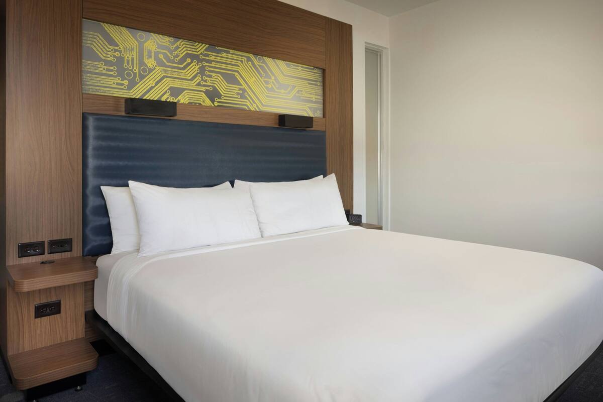 A hotel room with a large bed, wooden headboard, and a wall-mounted artwork.