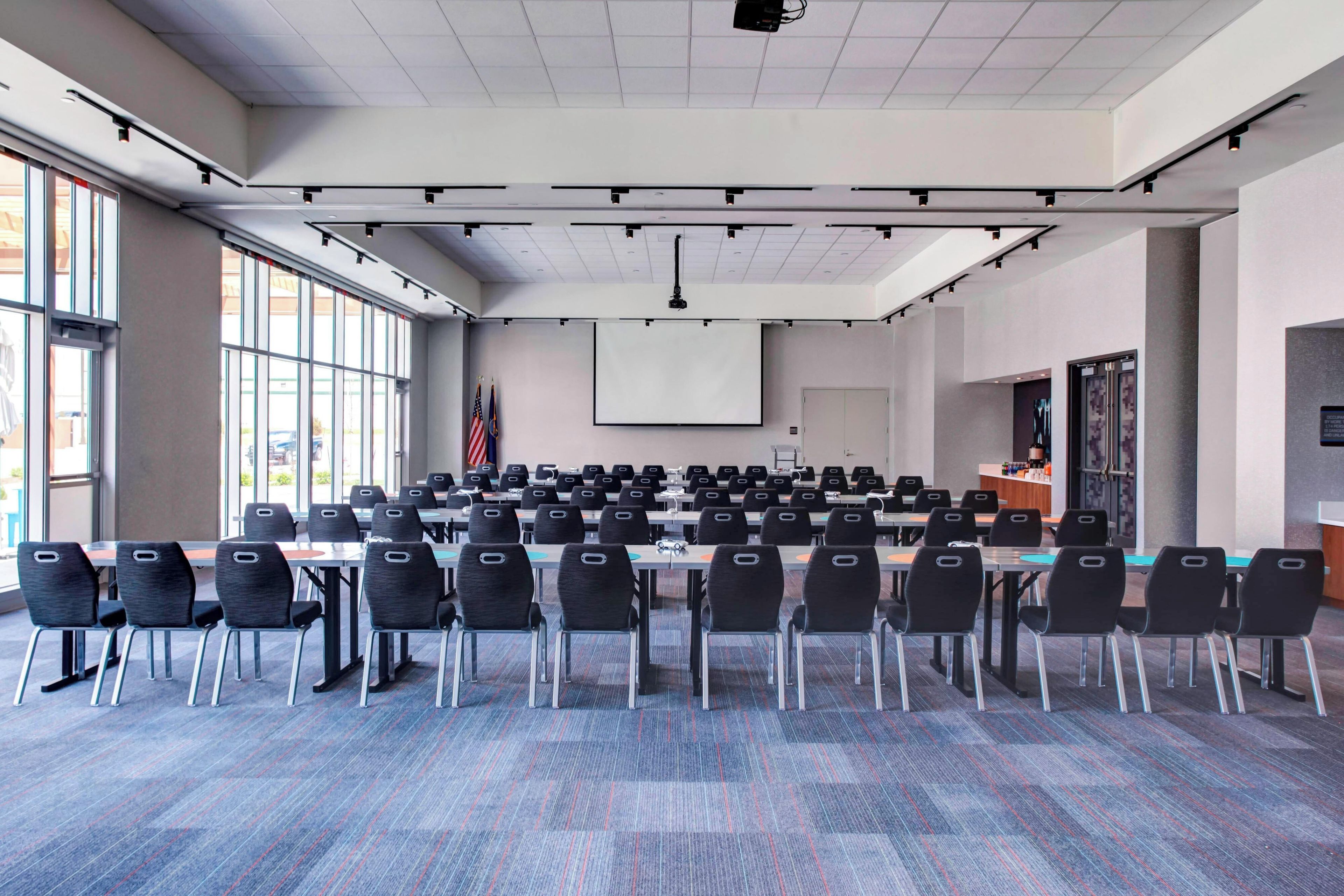 A conference room with rows of chairs, a projector screen, and flags.