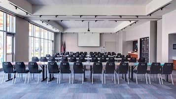 A conference room with rows of chairs, a projector screen, and flags.