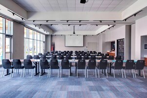 Un salón de conferencias con filas de sillas, una pantalla para proyector y banderas.