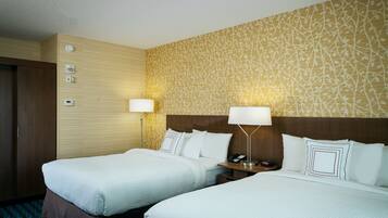 A hotel room with two beds, a wooden headboard, a patterned wall, and a nightstand with a lamp and phone.