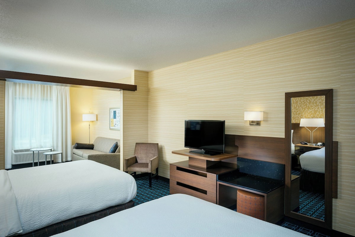A hotel room with two beds, a TV, a desk, and a chair.