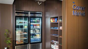 Un mercado de barrio con dos refrigeradores llenos de bebidas y aperitivos, y estantes con productos envasados.