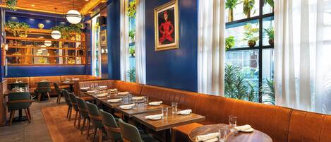 Un restaurante con mesas y cabinas, una pared azul con un cuadro y plantas.