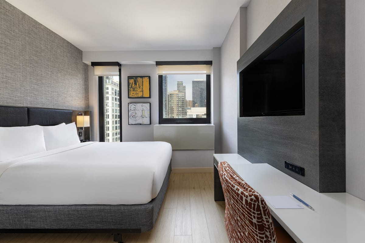 Ein modernes Hotelzimmer mit einem großen Bett, einem Schreibtisch, einem Fernseher und Blick auf die Stadt.