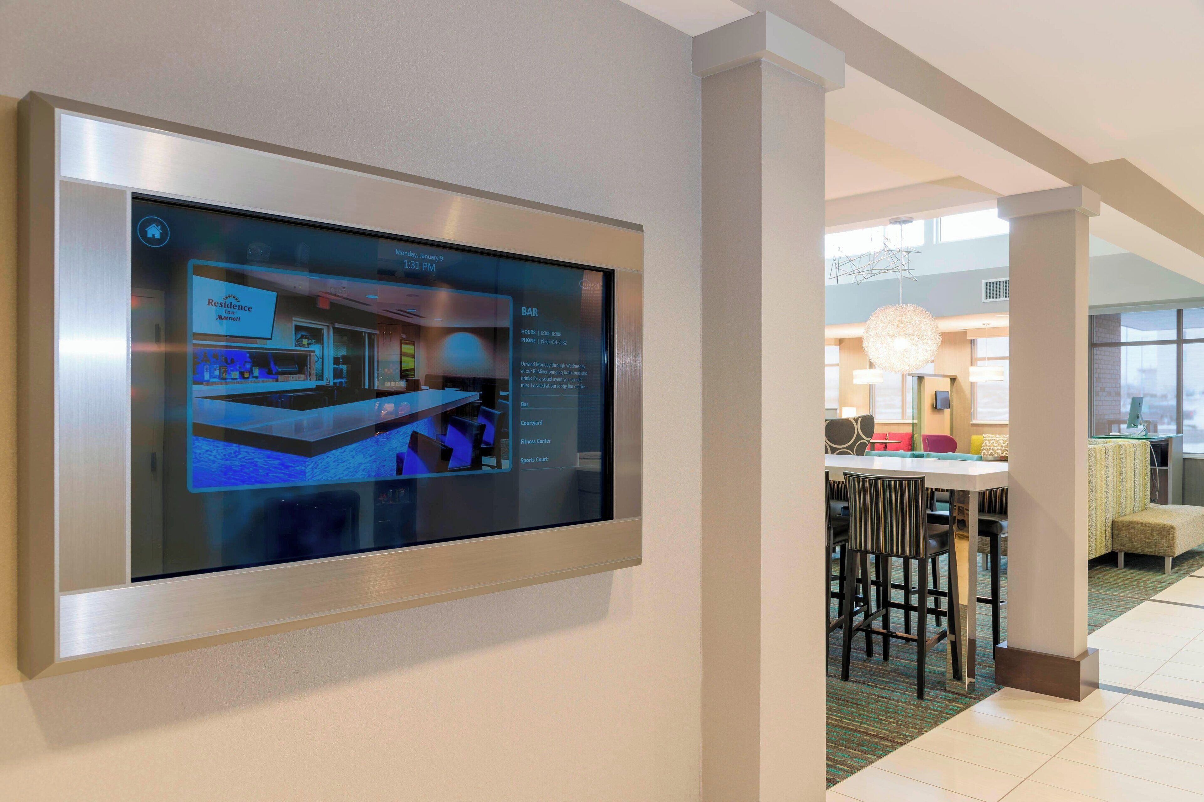 Un display digitale nella hall di un hotel, sullo sfondo si vede un'area bar e posti a sedere.