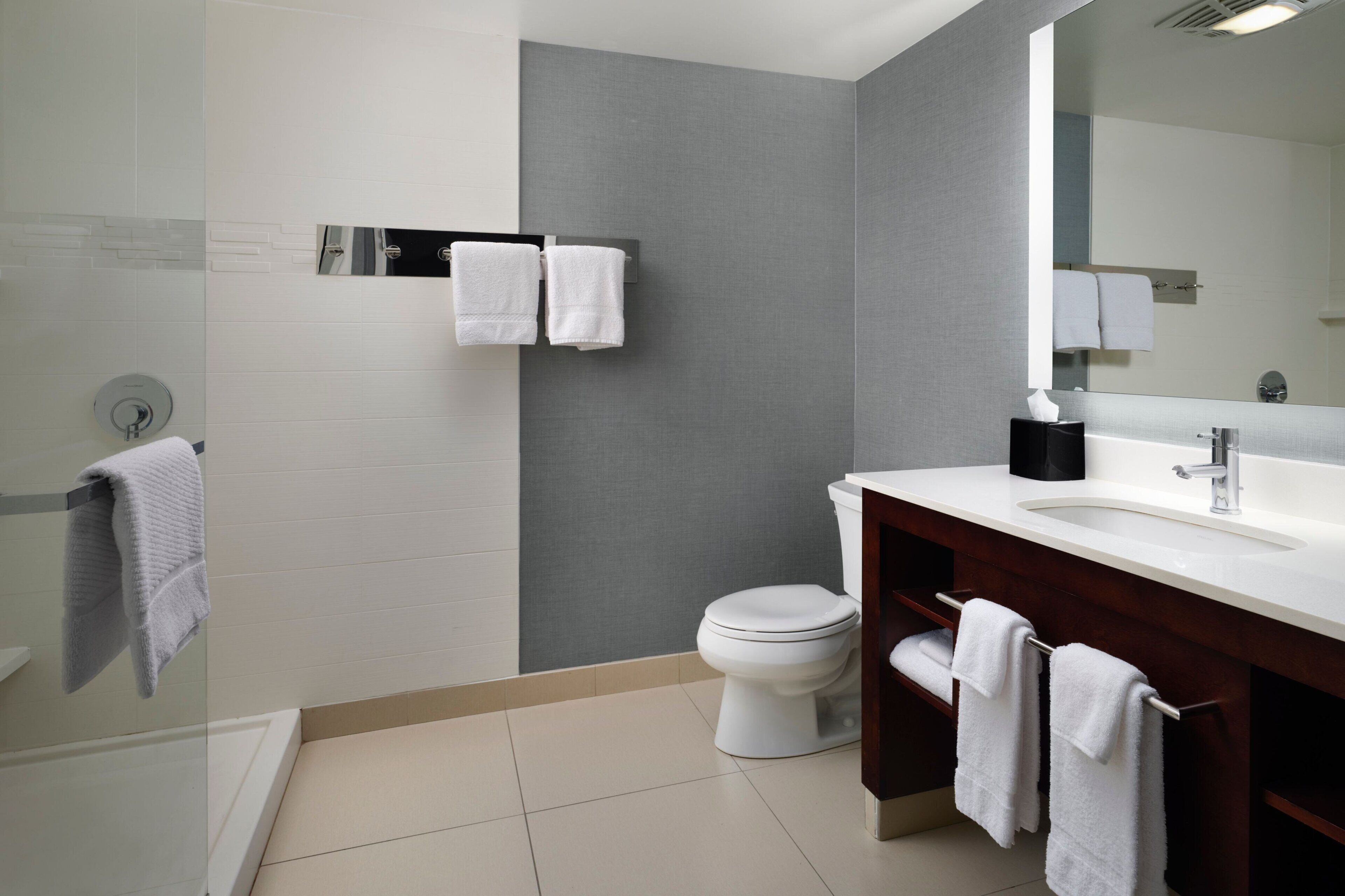 A modern bathroom with a white toilet, a glass shower enclosure, a white sink with a dark vanity, and a large mirror.
