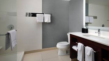 A modern bathroom with a white toilet, a glass shower enclosure, a white sink with a dark vanity, and a large mirror.