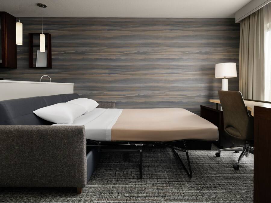 A modern hotel room with a bed, a desk, and a chair.