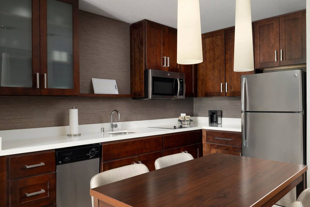 Una cucina moderna con mobili in legno scuro, elettrodomestici in acciaio inossidabile, un piano di lavoro bianco e un tavolo da pranzo in legno.