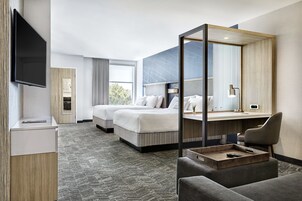 Habitación de hotel con dos camas, un escritorio, una silla, un televisor y un espejo grande.