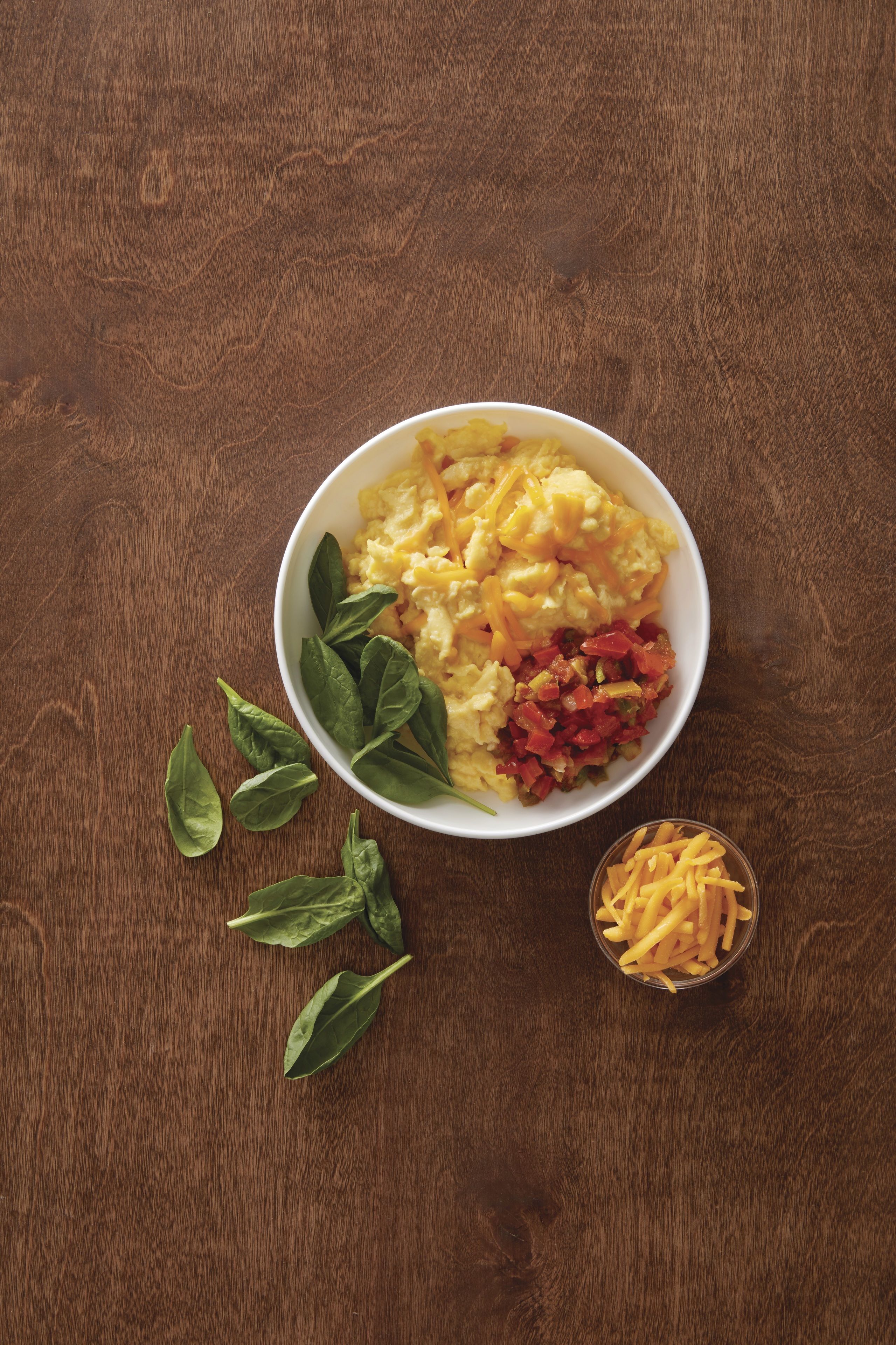 A bowl of food with spinach leaves and a small container of fries on a wooden surface.