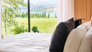 A bedroom with a large window offering a view of a grassy field and hills. - Mt Michael Lodge (Lowburn)