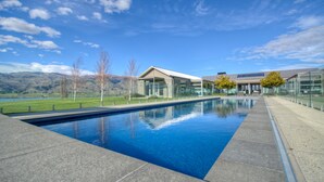 A modern pool area with a clear blue pool, surrounded by a paved deck and glass walls. - Mt Michael Lodge (Lowburn)