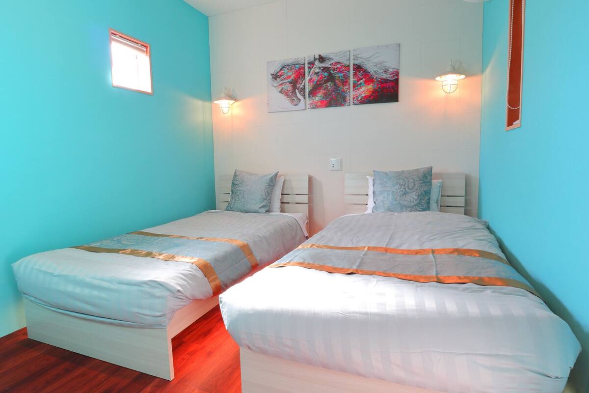 Une chambre avec deux lits, chacun doté d’une tête de lit, d’une petite fenêtre et d’un luminaire fixé au mur.