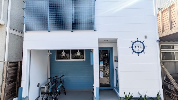 Un bâtiment à deux étages avec un balcon bleu, un garage avec une porte bleue et une enseigne à thème nautique sur le mur.