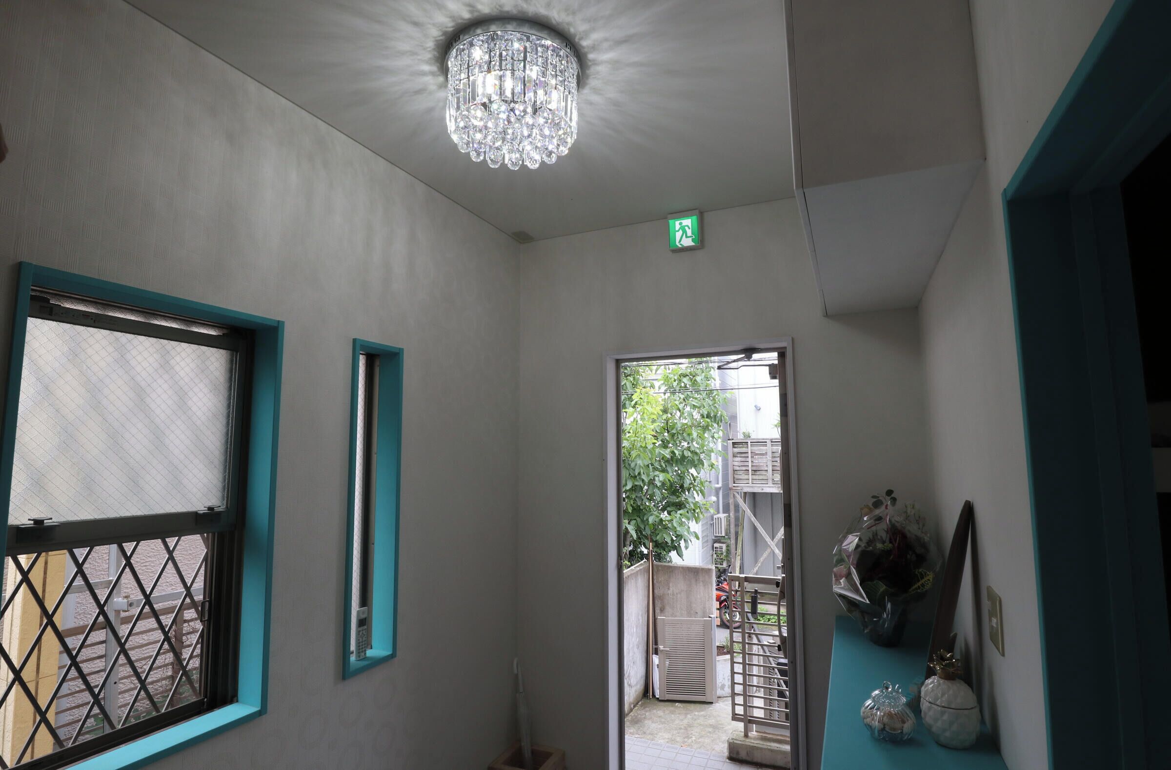 A hallway with a chandelier, a door with a green exit sign, and a window with a metal grille.