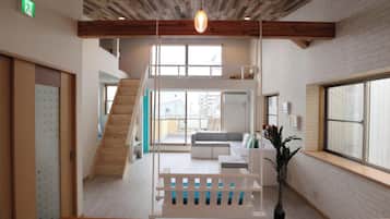 Un interior moderno con una escalera de madera, una zona de estar y ventanas amplias.