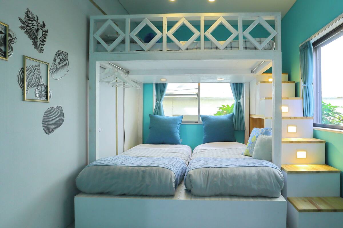 Ein Zimmer mit zwei Betten, einem Fenster mit Vorhängen und Blick auf Grünfläche.
