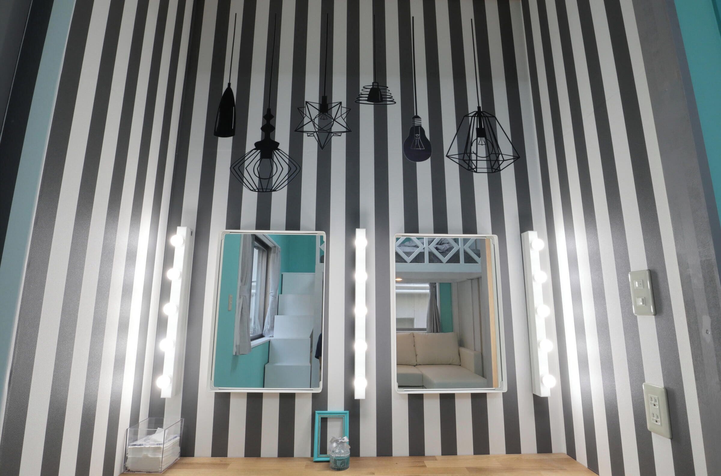 Une salle de bain avec des murs à rayures, deux miroirs et plusieurs luminaires.