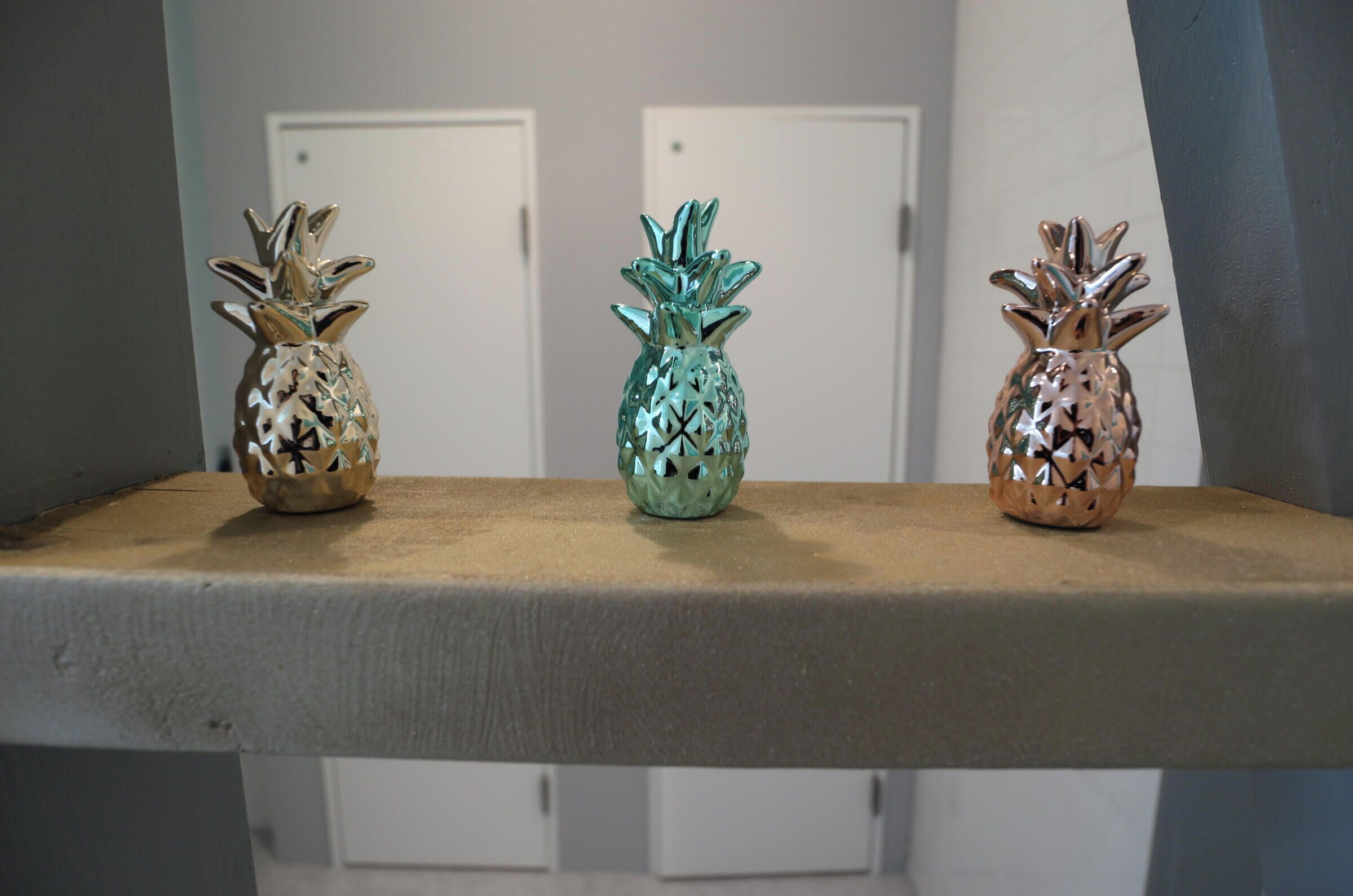 Trois vases décoratifs en forme d’ananas, disposés sur une étagère.